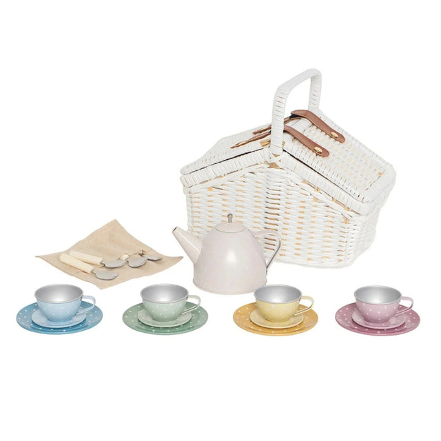 A children's tea time tea set featuring a white wicker picnic basket with wooden handles, a pale pink  teapot, four small pastel-colored teacups and saucers in blue, green, yellow, and pink, a beige napkin, and 4 spoons on a white background.