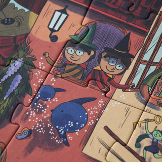 A close-up of a completed jigsaw puzzle showing whimsical illustrated characters and objects, including two children in witch hats, blue birds, a lantern, and a goblin-like fairy figure, with puzzle-piece cutlines visible across the artwork.