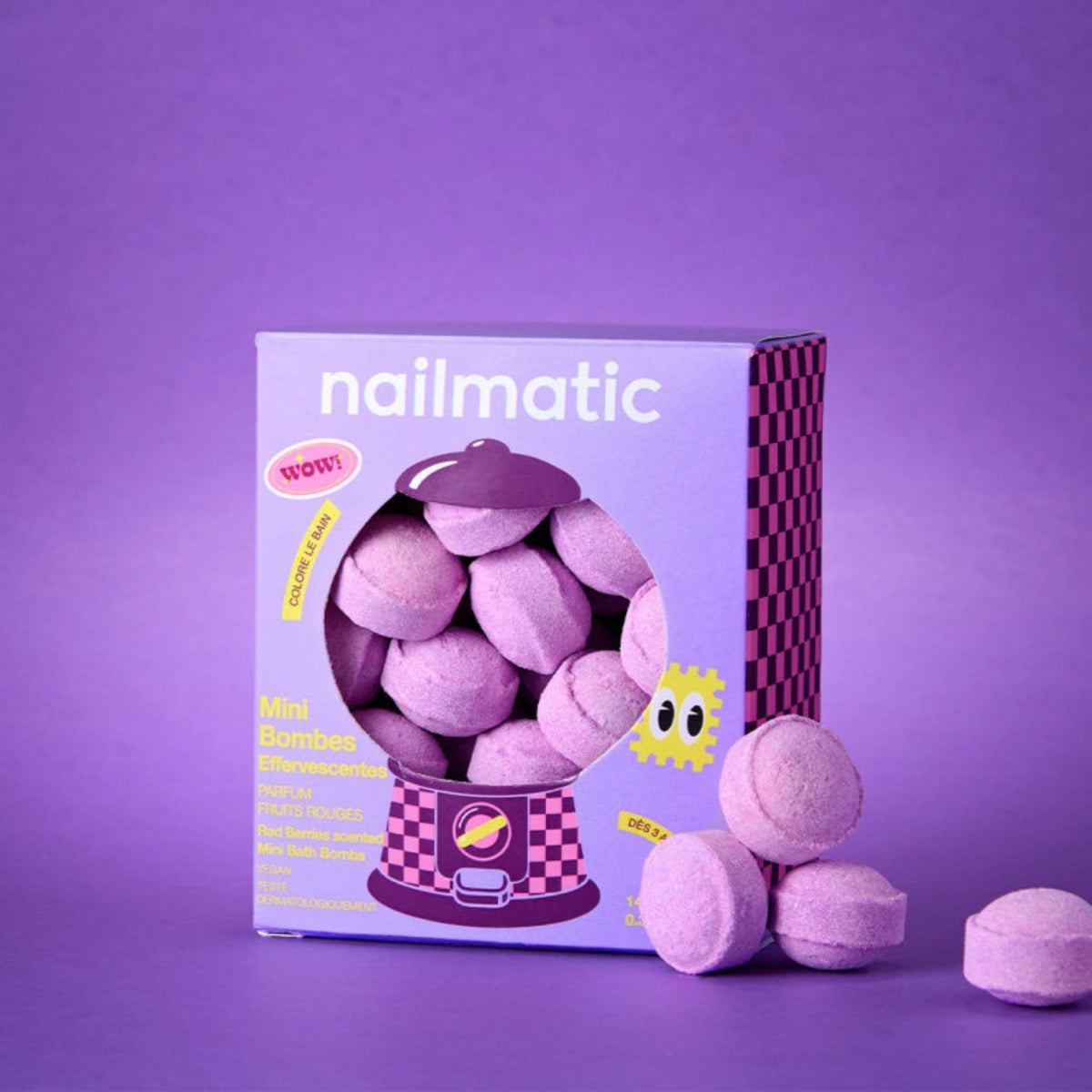 A box of Nailmatic Mini Bath Bombs - Berry Bloom, alongside several loose, round, lavender-colored bath bombs on a matching purple background.