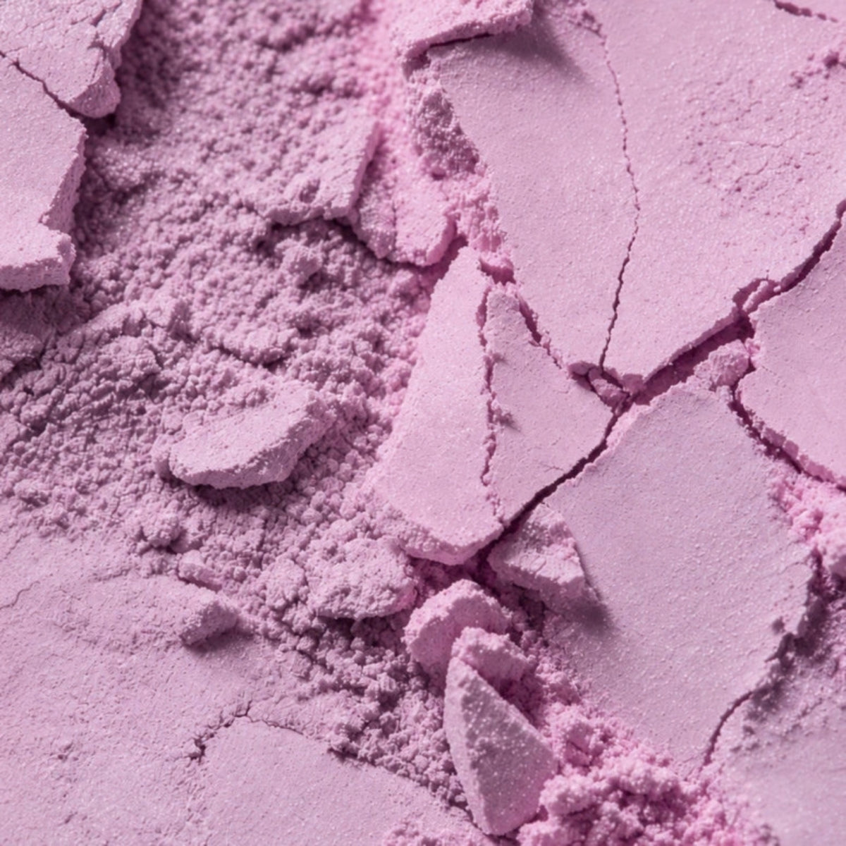 A close-up of loose and pressed light purple powder with visible cracked texture and fine particles.