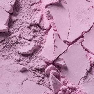 A close-up of loose and pressed light purple powder with visible cracked texture and fine particles.