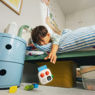 A young boy is leaning out of his bed as his Yoto Mini Palyer 4th Gen has fallen out, it is in mid-air as he grasps for it.